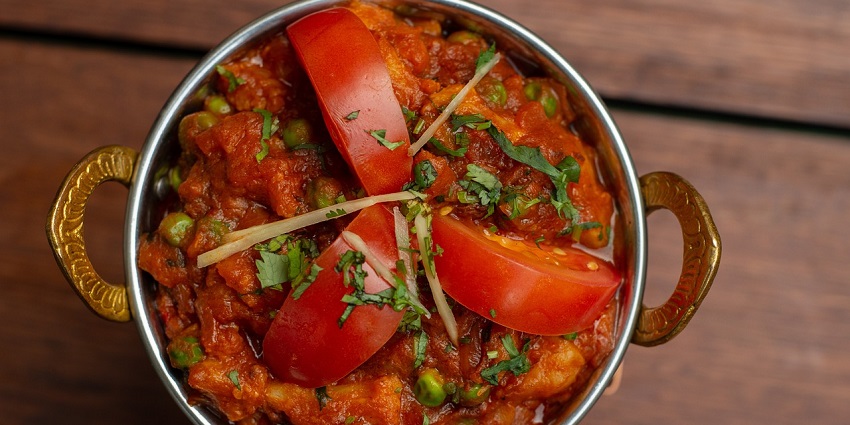 Traditional Indian chicken meal served in a silver bowl with tomato slices and coriander.