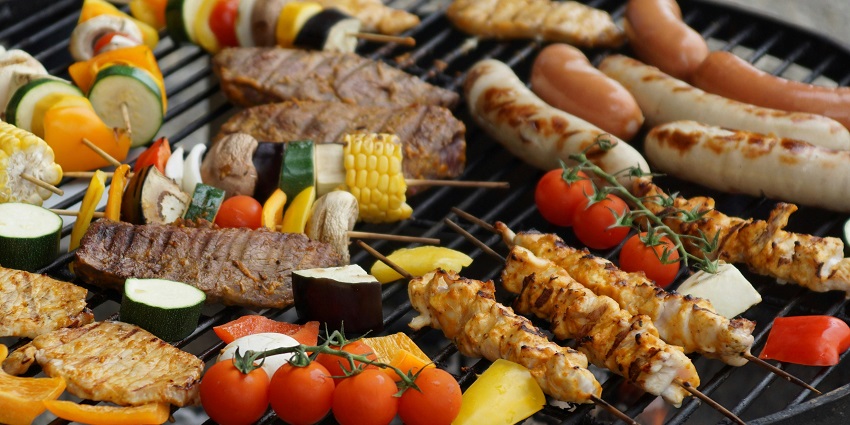 Skewers of meat and vegetables grilling over hot charcoal on a barbecue emitting smoke.