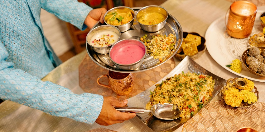 A person serving food on a stainless steel plate with different dishes on the table.