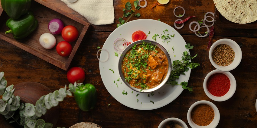 An image of an Indian dish of paneer with soup and spices all over the table.