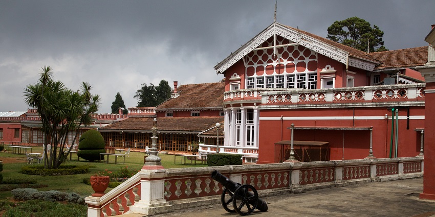 A view of Fernhills Palace Hotel in Ooty, a grand white building with a red roof set amid green gardens.