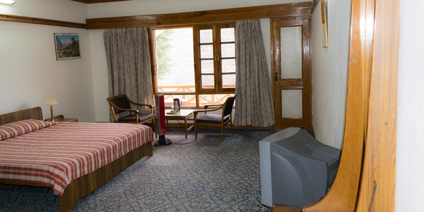 A hotel room with a neatly made bed, wooden furnishings, and a window showing a scenic view.