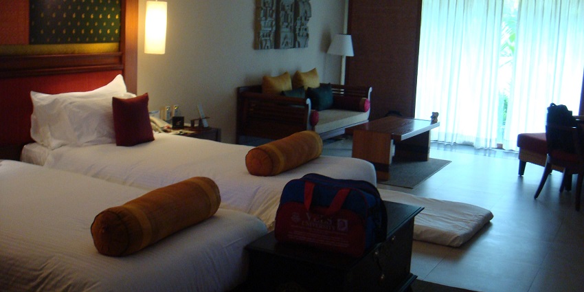 Hotel room with two beds, a sofa, a coffee table, and a large window with curtains.
