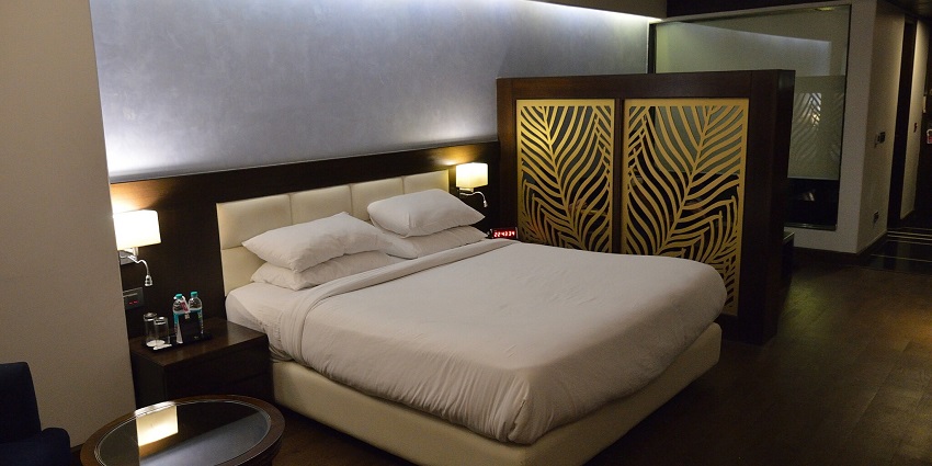 A hotel room with a neatly made bed, modern furnishings, cosy lights, and a wooden floor
