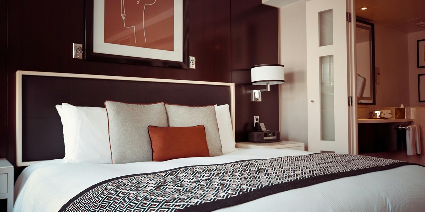 A bed with a grey bedspread and pillows in the room of a hotel in Jharkhand.