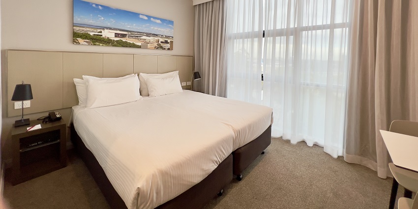 A hotel room with a comfortable bed, a painting and large windows with curtains.