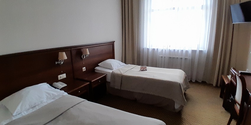 A hotel room with two single beds, wooden headboards, bedside tables, and a window