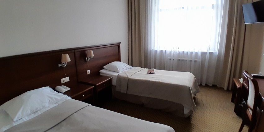 Hotel room with two single beds, modern furnishings, lamps beside the beds and a chair