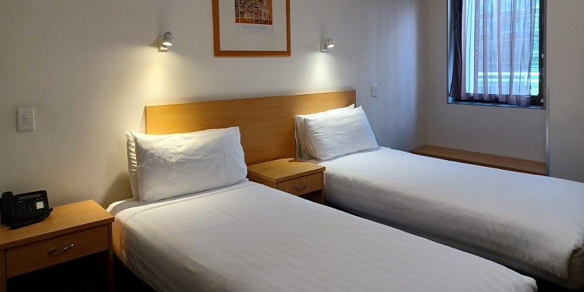 A hotel room with two beds, a painting hanging on the wall, a window and a telephone