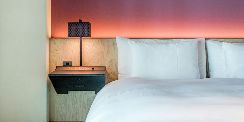 Cozy hotel room with neatly made bed and pillows and warm lighting of a bedside lamp.