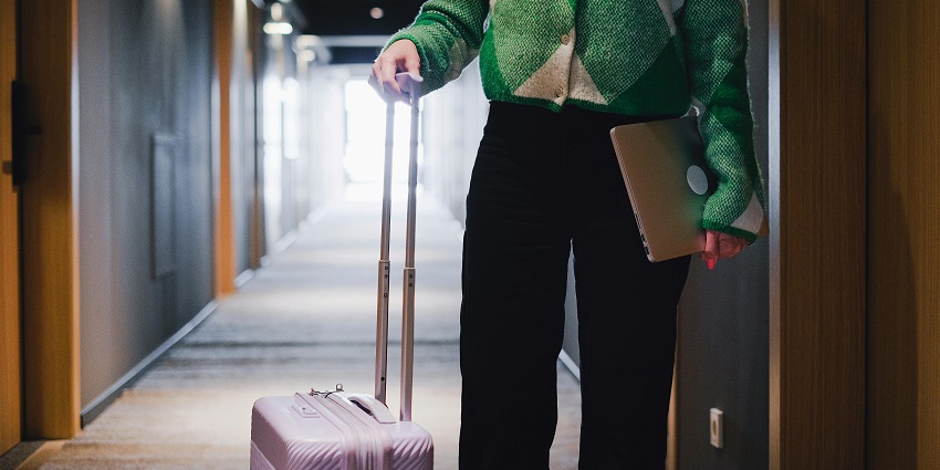 A person standing in the hallway with luggage and carrying a laptop in the other hand
