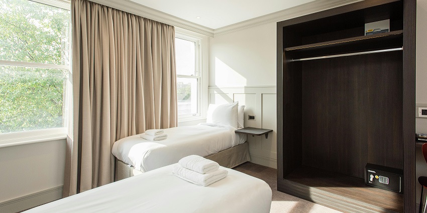 A room featuring two neatly arranged beds and a large window, near Chettipunniyam Temple.