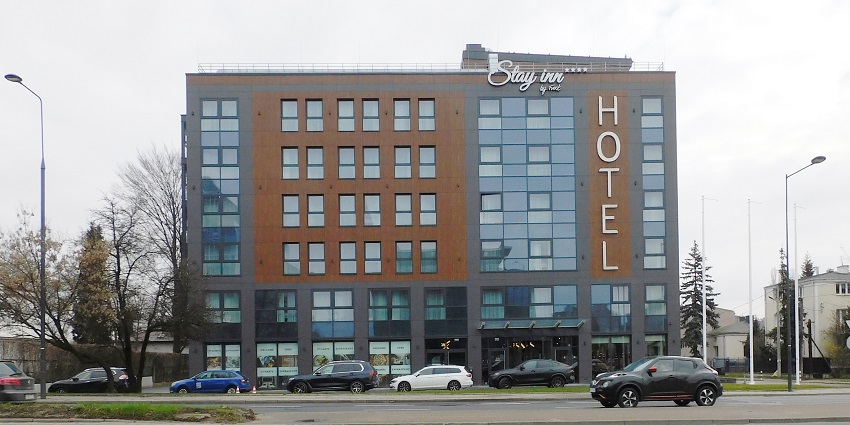 Front view of a Hotel featuring glass windows and various cars parked outside the hotel.