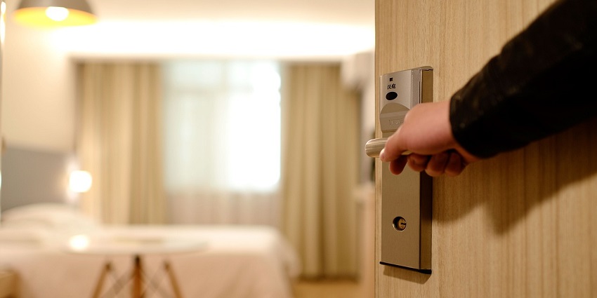 A person opening the door of a room with only one hand visible and a blurred background.
