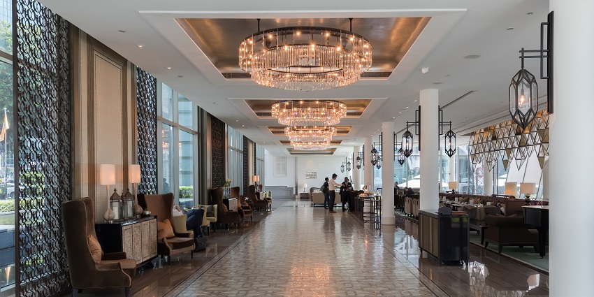 A hotel lobby with large chandeliers with people making inquiries and seating arrangements