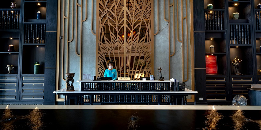 A picture of a receptionist standing in front of a hotel reception while performing check-in formalities.