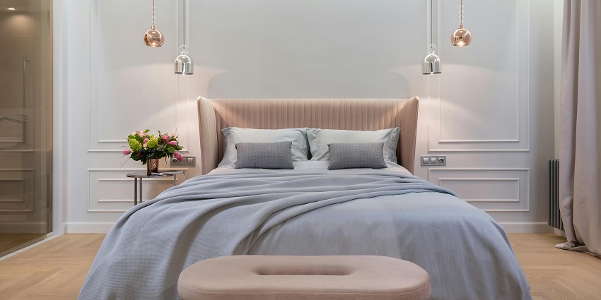This image depicts the inside of a hotel bedroom, with a bed next to a table and lamps