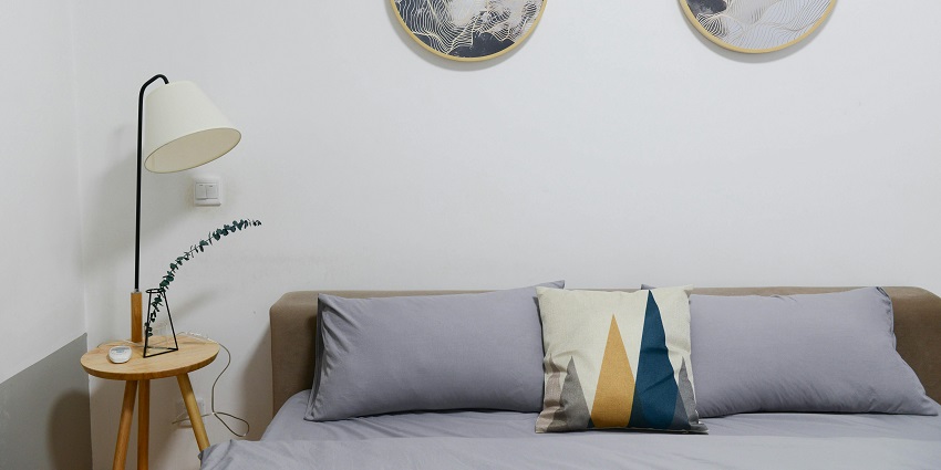 An image of a hotel bedroom with a brown hardwood bed and a grey bedding set.