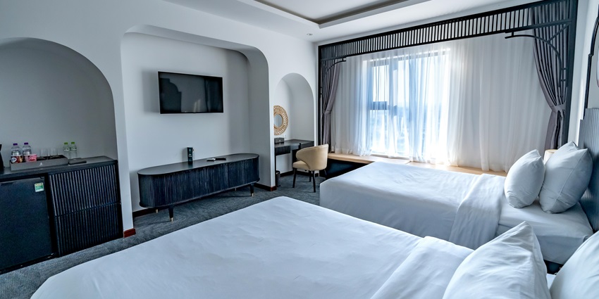 An image of two beds with natural light streaming into a contemporary hotel room setting.