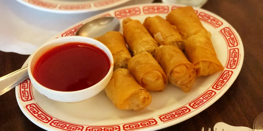 Spring rolls served on awhite plate and red sauce on the side - while covering the bottom of the roll with papers
