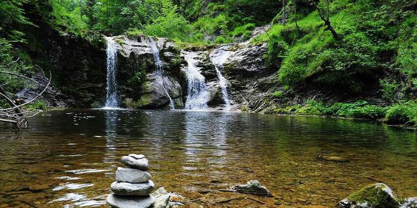 An image of a waterfall that pours into a pool, the pool has a rock cairn around the edges.