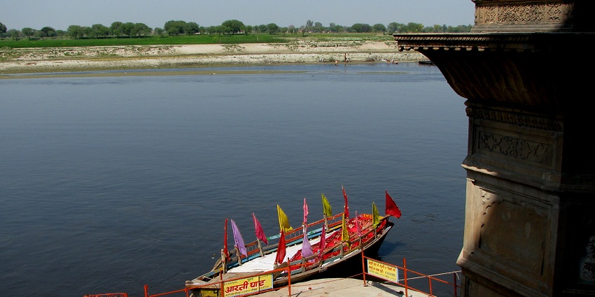 People at riverbank steps in Vrindavan, India, with Yamuna River and a tourist attraction