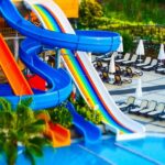 A swimming pool at the Nilansh Water Park featuring colourful water slides, surrounded by greenery.