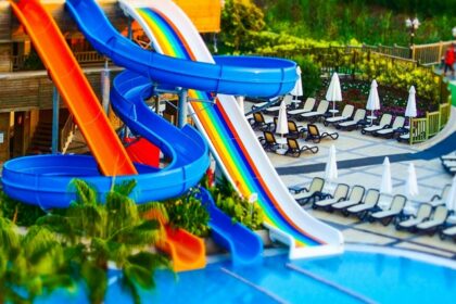 A swimming pool at the Nilansh Water Park featuring colourful water slides, surrounded by greenery.