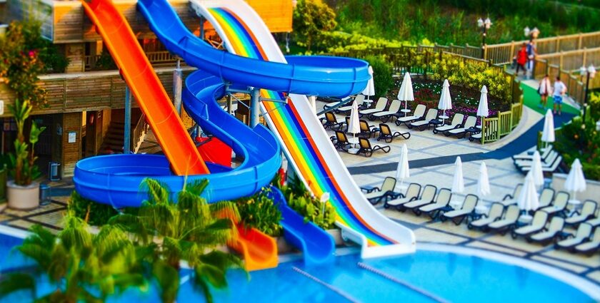 A swimming pool at the Nilansh Water Park featuring colourful water slides, surrounded by greenery.