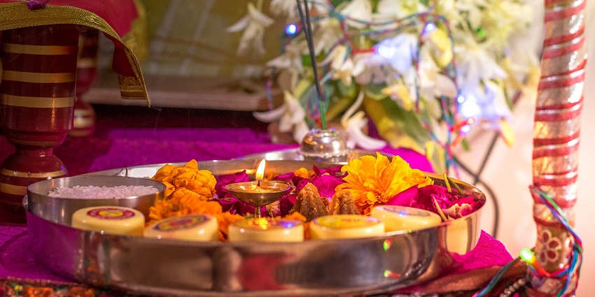 A puja thali, including a diya, prasad, and flowers as offerings during a puja.
