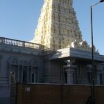 Murugan temple entrance with well-detailed pillars and motorcycles and cars parked.