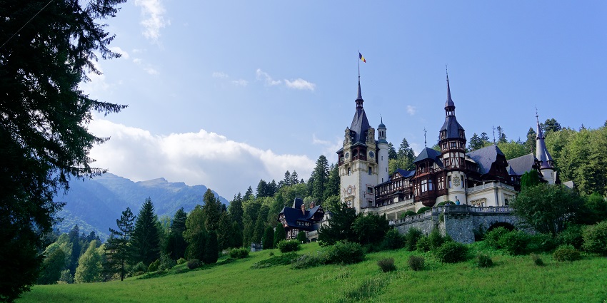 Peleș castle with detailed old-style architecture and a flag on top of the castle