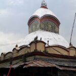 An image of Kalighat Temple entrance, surrounded by devotees and vibrant street vendors.