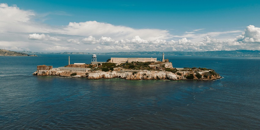 An aerial view of Alcatraz Island with museum building, blue waters and white clouds above
