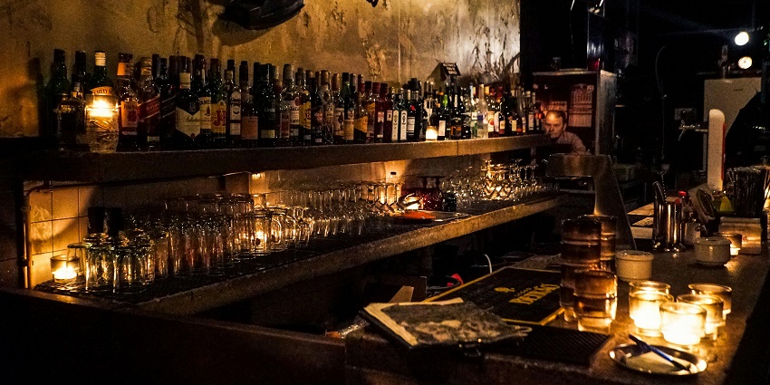 Old-fashioned bar counter with lined beverage bottles and bartender’s accessories