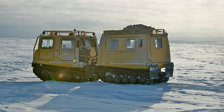 A snow vehicle with tracks parked on a snowy landscape in Alert, Nunavut, under a cloudy sky