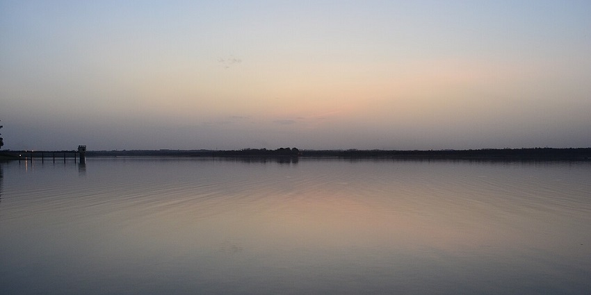 Ambazari Lake at sunset near Nagpur, bordered by trees and reflecting the sky.

