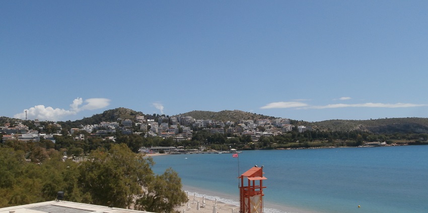 Vouliagmeni River beach with small mountains covered with buildings and structures