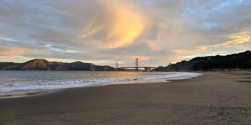 Baker Beach looks serene with a scenic view of the Golden Gate Bridge under a vibrant sky