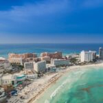 An aerial view of a beach in Cancun, showcasing a curved shoreline and soft, white sand