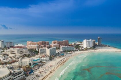 An aerial view of a beach in Cancun, showcasing a curved shoreline and soft, white sand