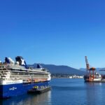 A view of a ship docked in a harbour surrounded by lush greenery, city view, and mountains.