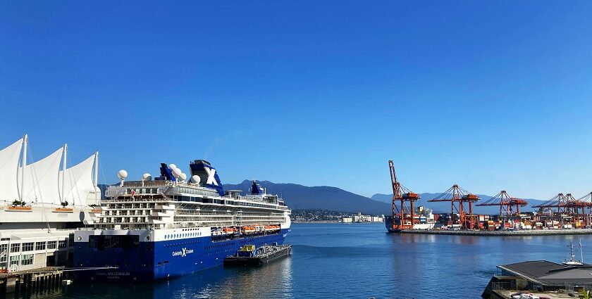 A view of a ship docked in a harbour surrounded by lush greenery, city view, and mountains.