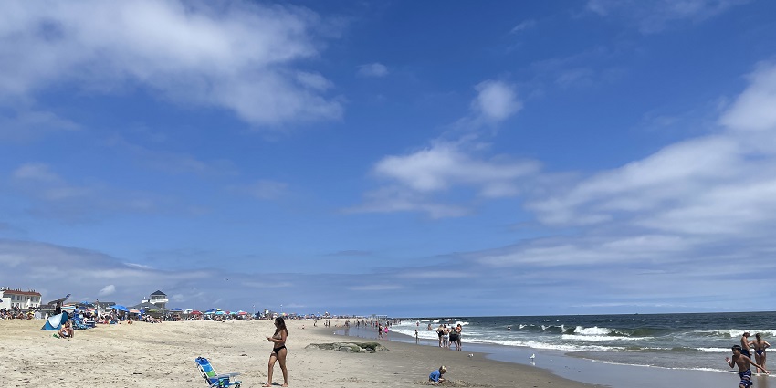 Wide sandy beach with scattered people and calm ocean waves looking north from Belmar Beach.