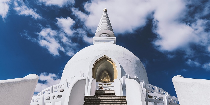 An image of a temple building with ornate architecture beneath a cloudy sky featuring detailed carvings.