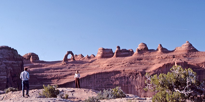 View of Delicate Arch in Arches National Park, with a clear blue sky and warm sunlight