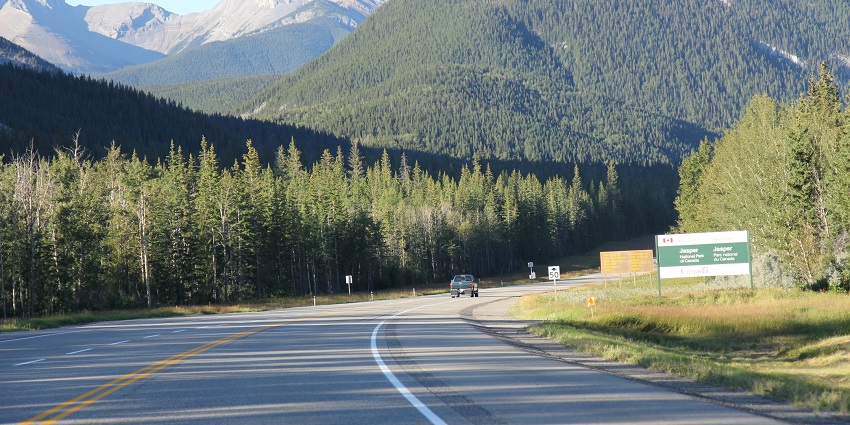 A scenic road leading into Jasper National Park, with a sign marking the entrance