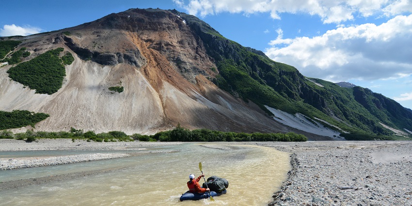 Vast Alaskan landscape with snow-capped mountains, green valleys, and a clear blue sky
