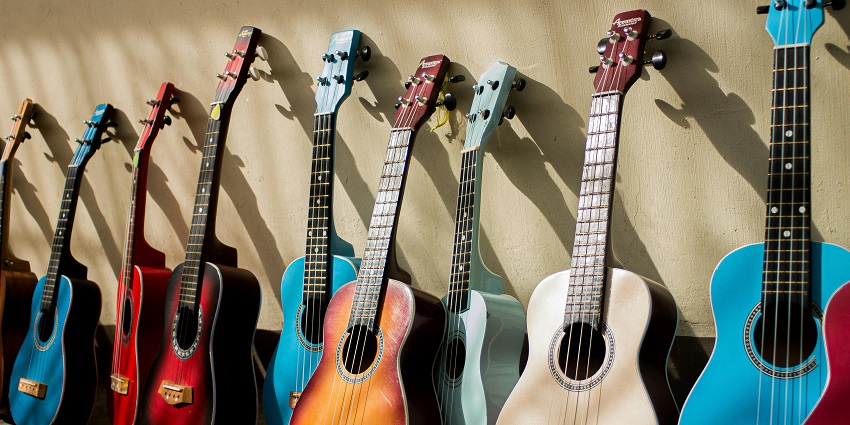 A display of assorted acoustic guitars in varying colours and sizes, arranged in a museum for display.