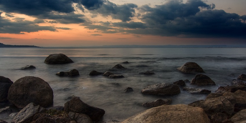 Black sea shoreline in the evening with stones of the sea under a cloudy sky and sunset